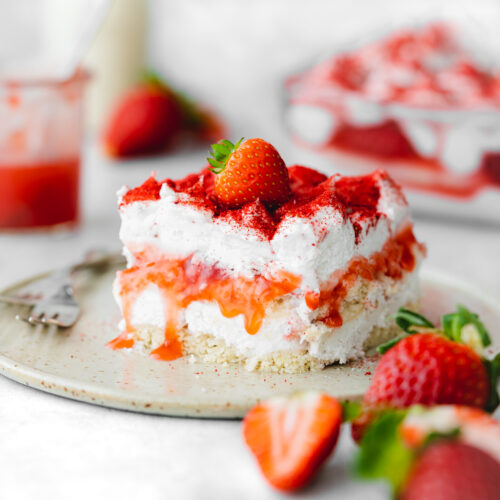 layered strawberry tiramisu on a plate with fresh strawberries and strawberry sauce.