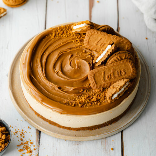 biscoff cheesecake with lotus biscuits on a ceramic plate and white wooden surface.