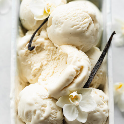 vegan vanilla ice cream scoops with vanilla pods and vanilla flowers in a powder blue ceramic dish.