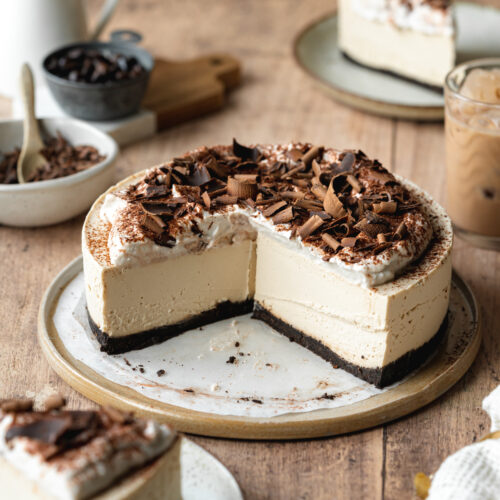 baileys cheesecake with cream and chocolate shavings on top of a ceramic plate with a glass of baileys next to it.