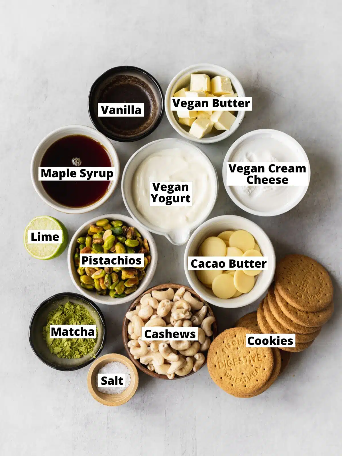 ingredients for matcha cheesecake measured out in bowls on a gray surface.