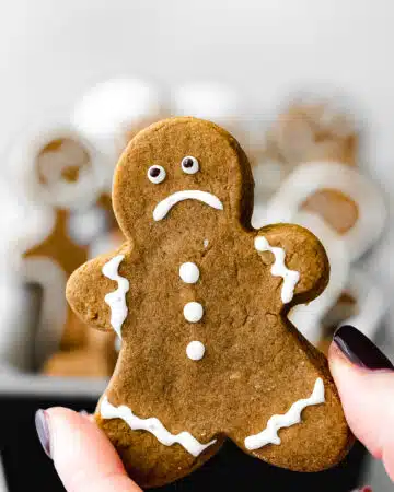 hand holding up a gingerbread cookie with a sad expression.