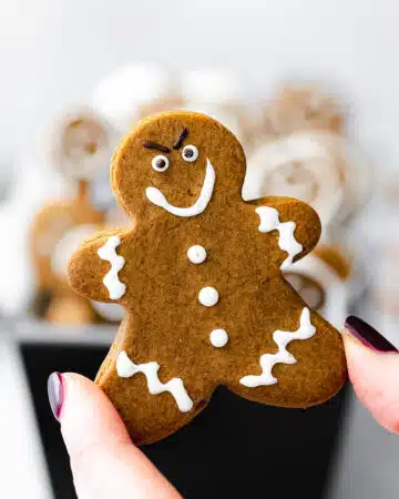 hand holding up a gingerbread cookie with a mischievous expression.