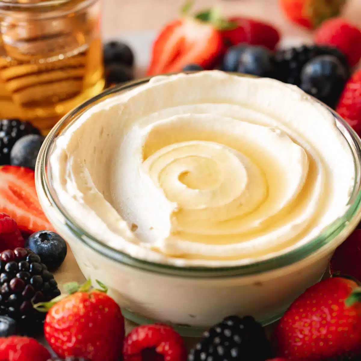 a glass pot of vegan mascarpone cheesecake with fresh berries and a pot of maple syrup in the background.