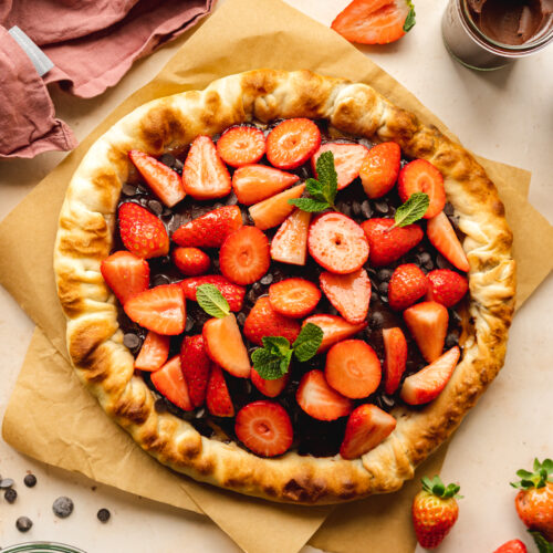 vegan dessert pizza with nutella and strawberries on a sheet of brown baking paper.