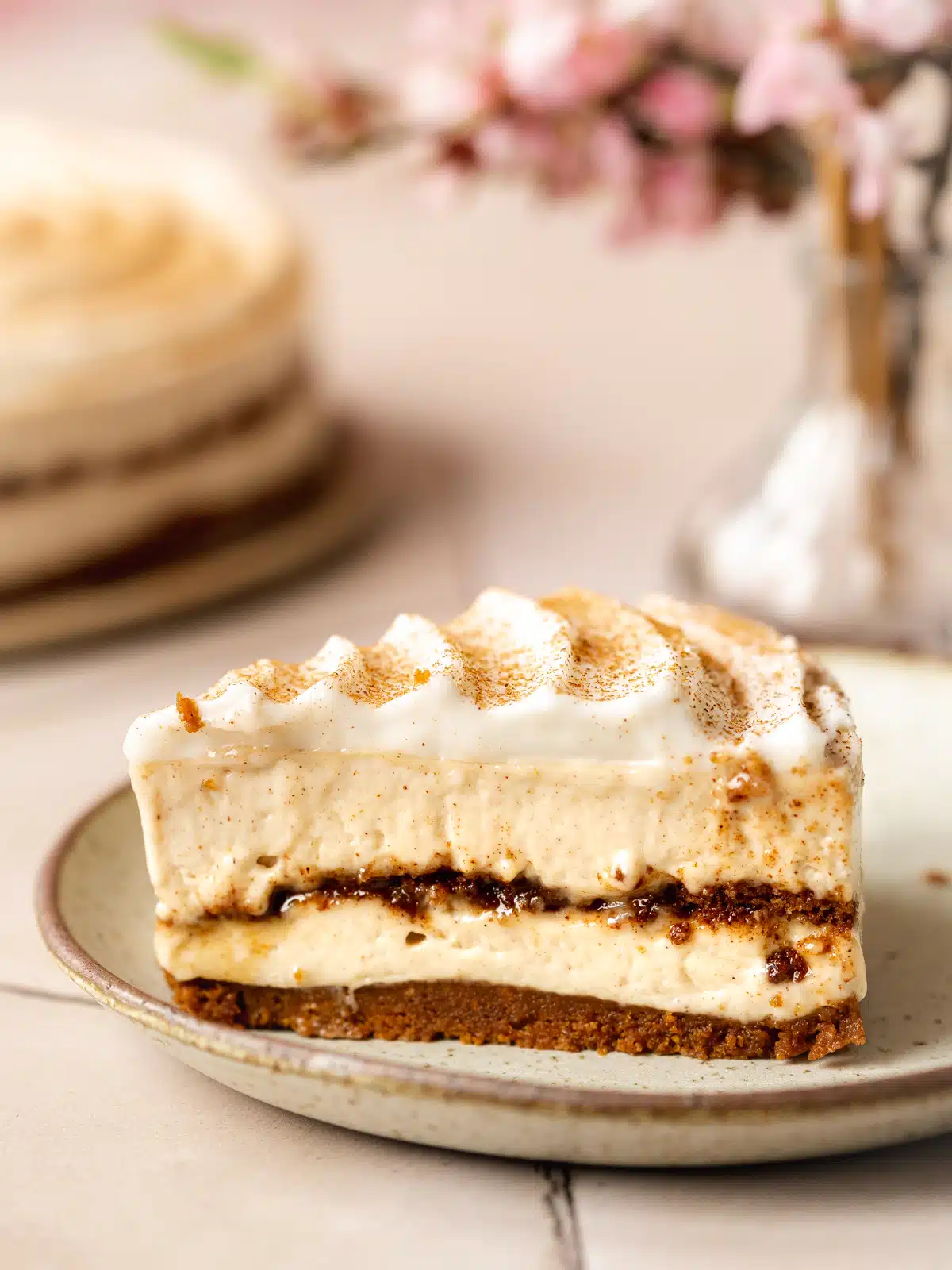 Sideways shot of a slice of no-bake vegan cinnamon roll cheesecake on an earthenware plate, showing the cinnamon sugar layer clearly in the middle.