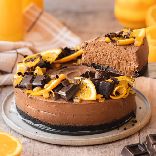 45 degree angle hero shot of a completed no-bake chocolate orange cheesecake on a serving plate with a pie server removing a slice from the right side.