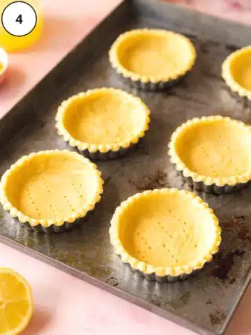 Sheet pan with 6 mini tart pans filled with a thin layer of rolled out vegan tart dough and pricked with a fork.