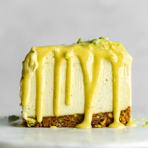 a slice of vegan pistachio cheesecake with pistachio ganache dripping down the sides.