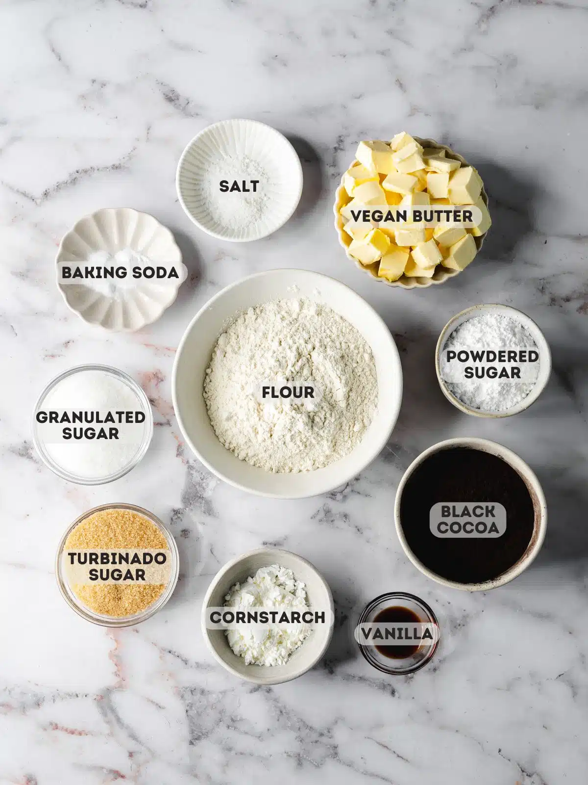 ingredients for vegan oreos measured out in bowls on a gray marble surface.