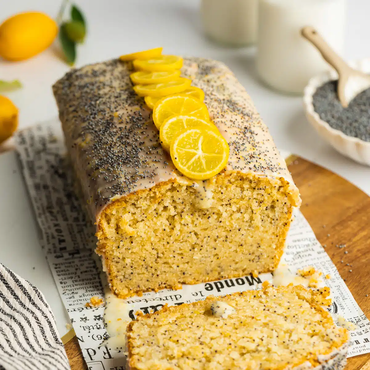 lemon poppy seed loaf with a slice taken from it on a wooden cutting board.