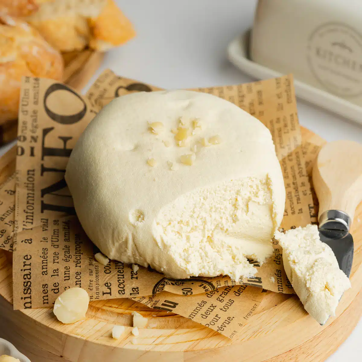 a round of macadamia cheese on some newspaper with a knife and a smear of cheese on it.